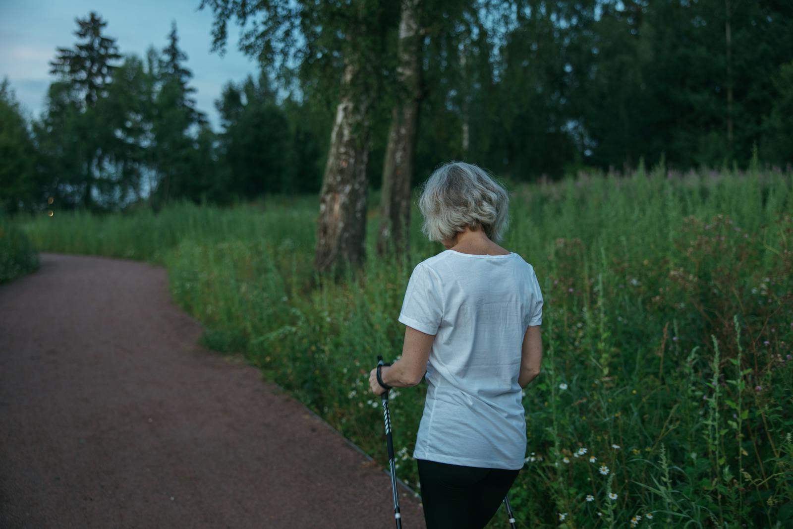 An active adult over 60 walking confidently outdoors on a bright day while practicing a simple supported balance exercise with a friendly instructor.